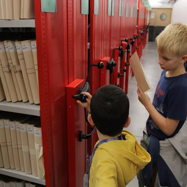 Enfants manipulant des rayonnages mobiles aux Archives départementales de l'Isère © Archives départementales de l'Isère